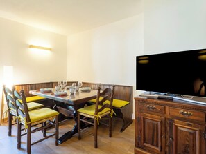 Zona pranzo con tavolo in legno, sedie e televisore su un mobile.