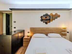 A modern hotel room with a wooden headboard, a bed with white linens, a nightstand with a lamp, a wall-mounted hexagonal light fixture, and a wooden wardrobe. - La Torre a Dorio by Interhome (Dorio)