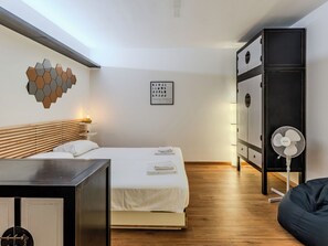 Ein Schlafzimmer mit Bett, Nachttisch, Kleiderschrank und einem Standventilator.