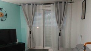 A living room with a sectional sofa, a TV, and a ceiling light fixture. - Escale Zen & Loggia: 5 min from the train station (Direct Paris) + Parking (Évry-Courcouronnes)