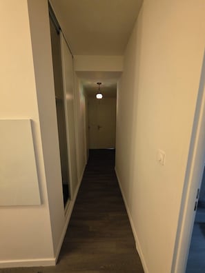 A narrow hallway with a dark wooden floor, white walls, and a ceiling light fixture. - Escale Zen & Loggia: 5 min from the train station (Direct Paris) + Parking (Évry-Courcouronnes)