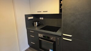 A compact kitchen with a built-in oven, a stovetop, and a refrigerator. - Escale Zen & Loggia: 5 min from the train station (Direct Paris) + Parking (Évry-Courcouronnes)