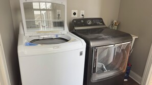 Un lave-linge et un sèche-linge à chargement frontal, installés dans une buanderie avec une fenêtre au-dessus du lave-linge.