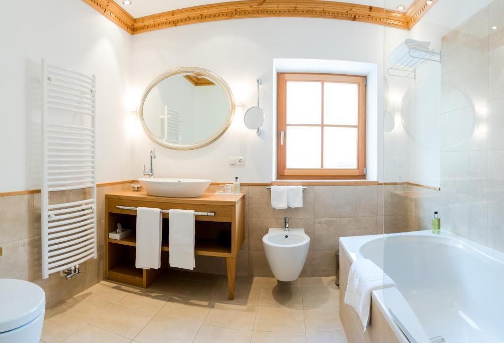 Een moderne badkamer met een vrijstaand bad, een ronde spiegel, een toilet en een houten wastafel met een wasbak en handdoekhouder.