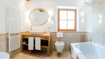 Een moderne badkamer met een vrijstaand bad, een ronde spiegel, een toilet en een houten wastafel met een wasbak en handdoekhouder.