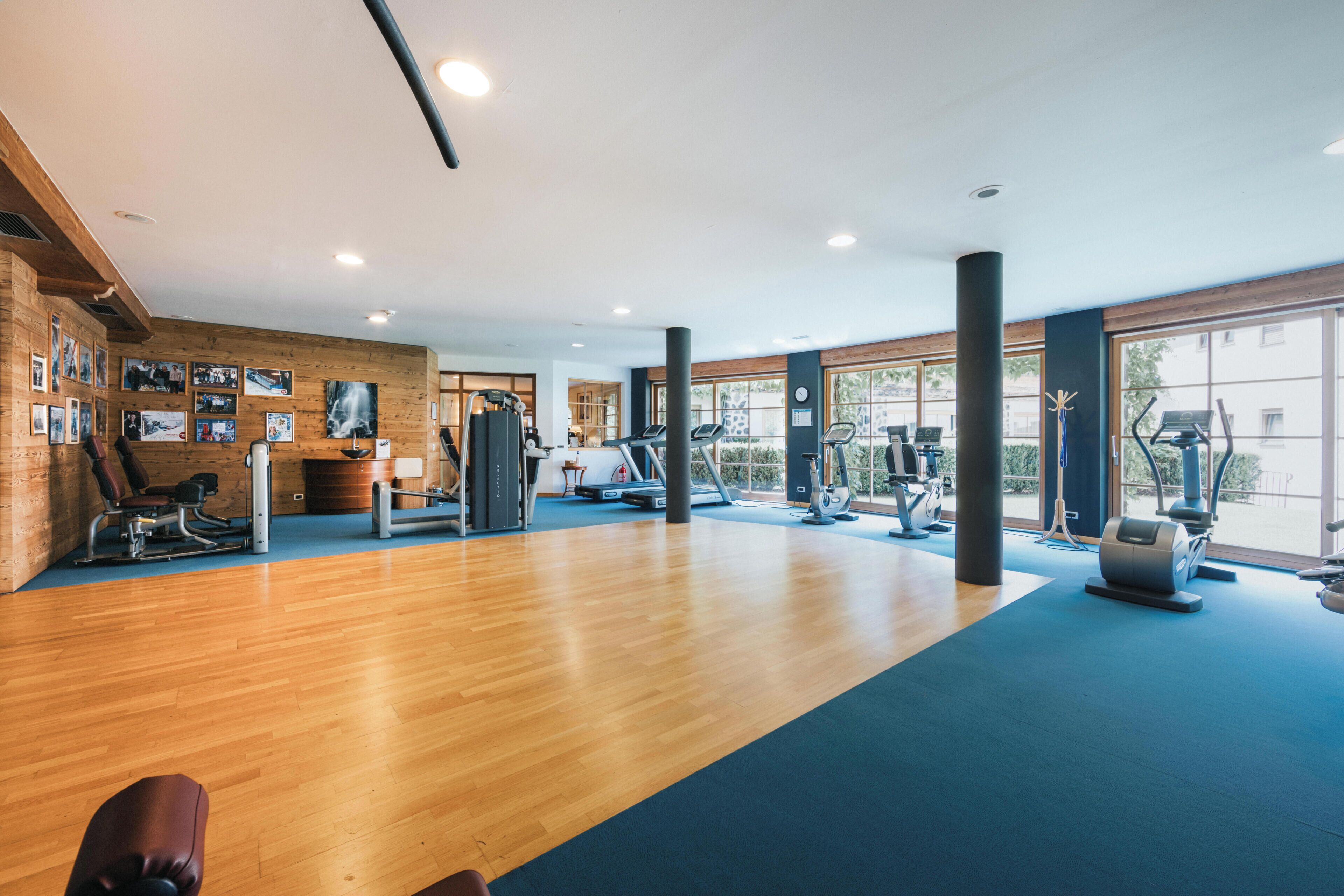 A gym with exercise equipment, wooden flooring, and large windows.