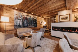 A cozy room with a fireplace, plush seating, and a large painting on the wall. -  Vitalhotel Dosses (Santa Cristina Val Gardena)