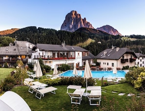 A hotel with a swimming pool, lounge chairs, and a mountain view. -  Vitalhotel Dosses (Santa Cristina Val Gardena)