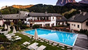 Hotel com piscina, espreguiçadeiras e montanhas ao fundo.