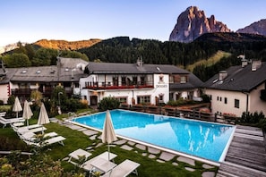Un hotel con piscina, sillones de descanso y montañas al fondo.
