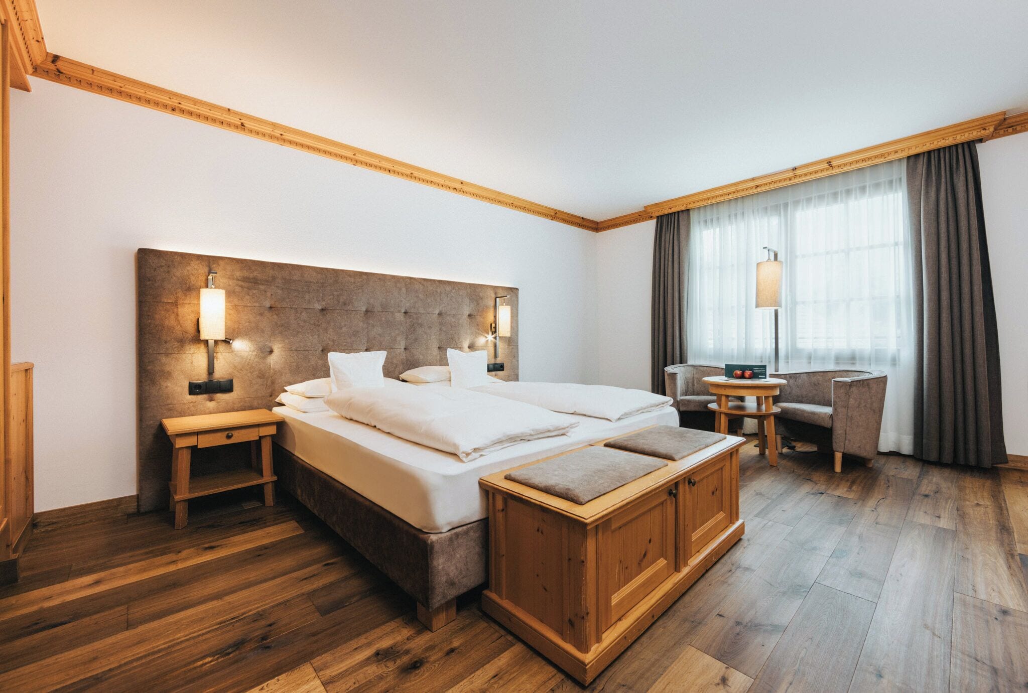A hotel room with a large bed, bedside tables, a wooden bench, a desk, and a chair.