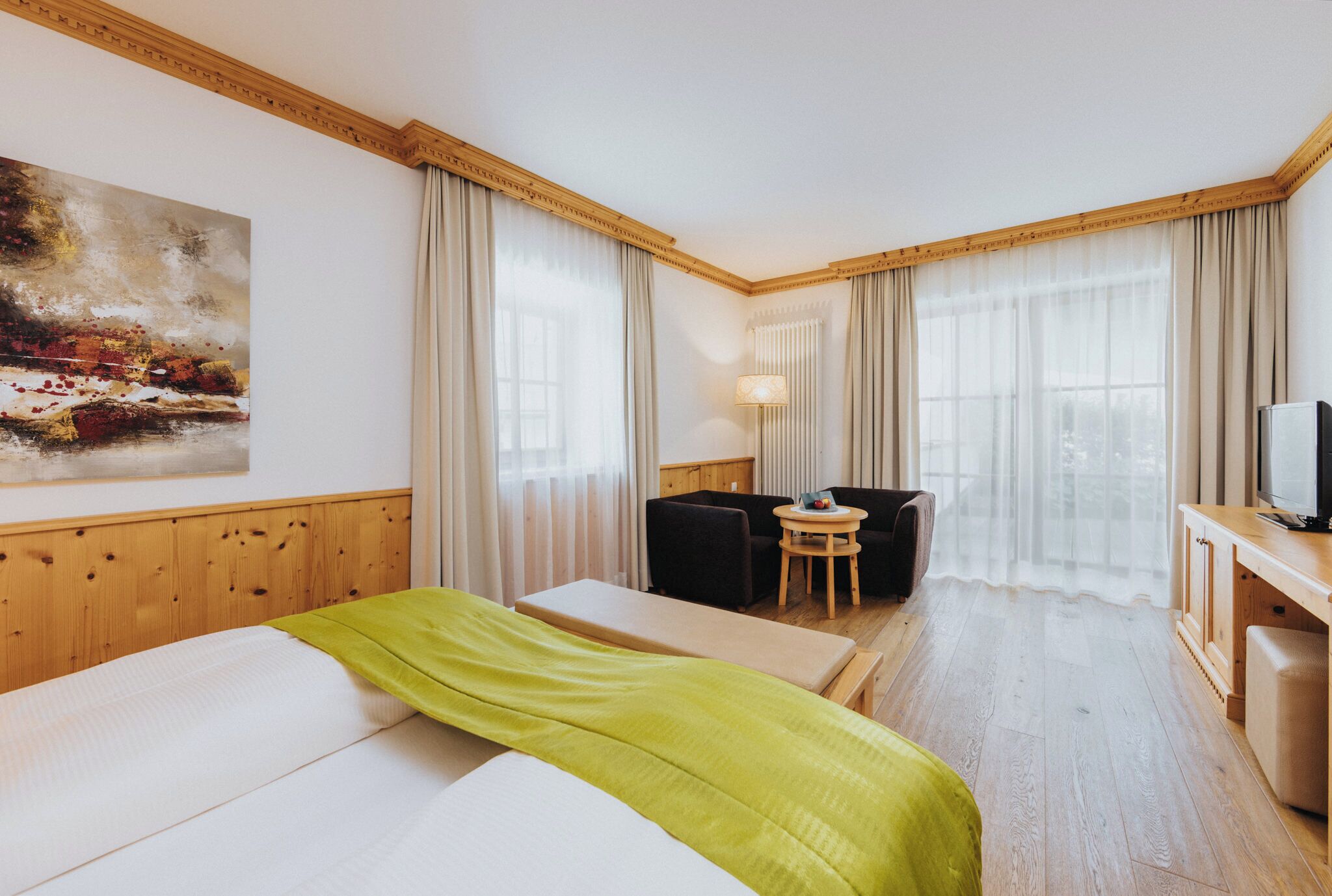 Habitación de hotel con cama, escritorio con televisor, silla, mesita y un cuadro en la pared.