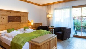 Quarto de hotel com cabeceira de madeira, cama com roupa de cama verde, mesa de cabeceira com abajur, uma cadeira e vista para o exterior através de grandes janelas.
