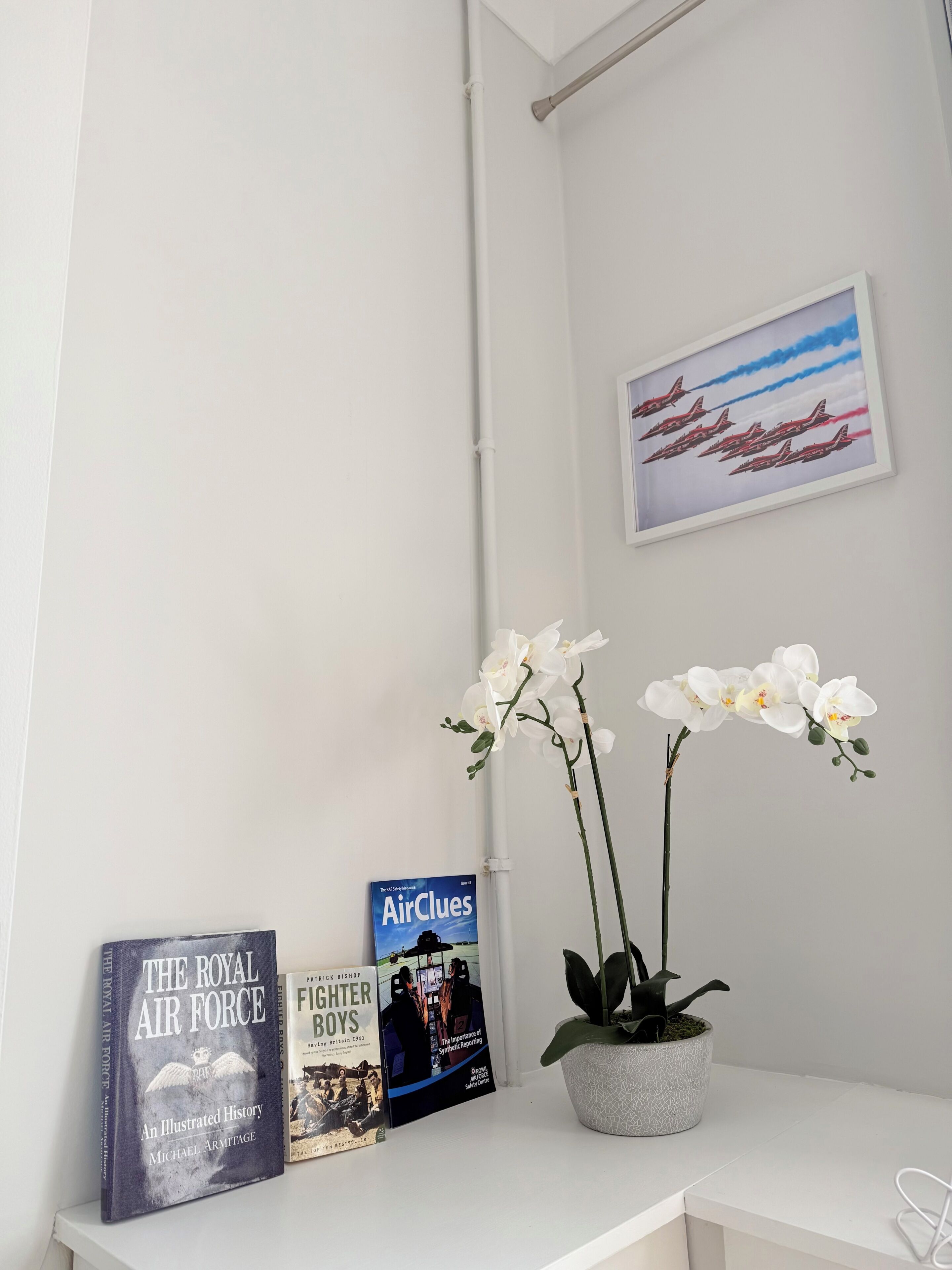 A white shelf with books, a framed picture, and white orchids.