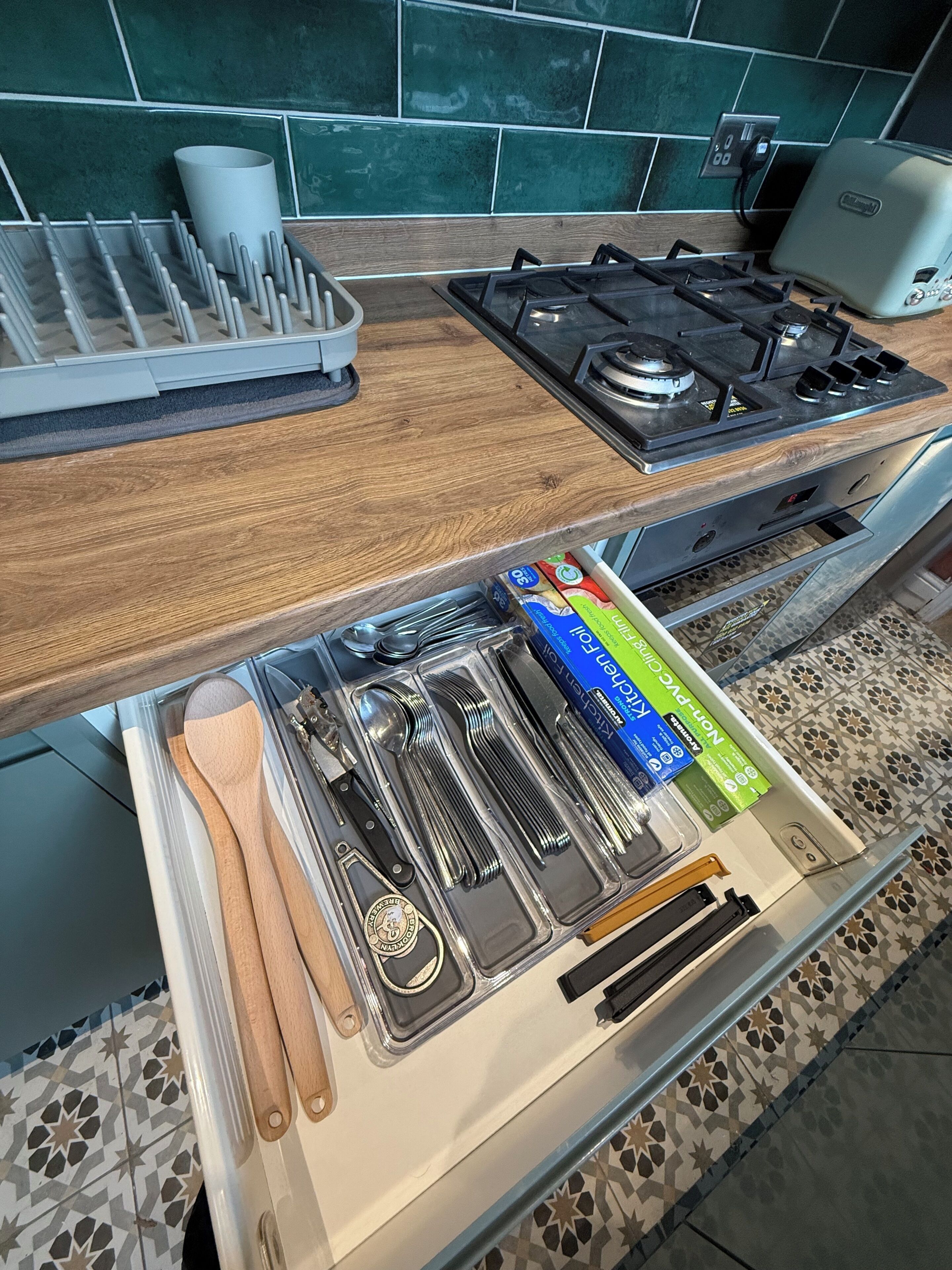 A kitchen with a wooden countertop, a gas stove, and a drawer with utensils and kitchenware.
