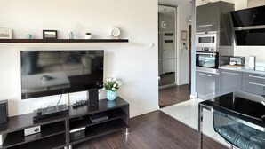 A modern living room with a flat-screen TV, dark wood flooring, and a minimalist design. - Bora Premium by Grand Apartments (Sopot)