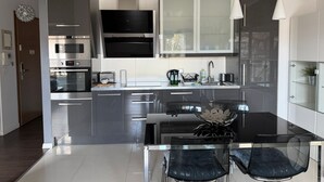 A modern kitchen with stainless steel appliances, a glass dining table, and a built-in TV. - Bora Premium by Grand Apartments (Sopot)