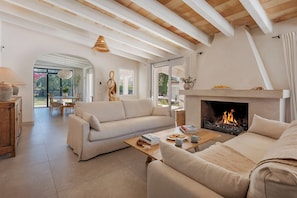 A living room with a fireplace, a sofa, a coffee table, and a dining area with natural light. - La Canova - Swimming Pool | Terrace | Mallorca (Mallorca)