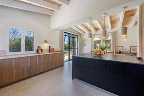 A modern kitchen with a large island, wooden cabinetry, and a view of the outdoors. - La Canova - Swimming Pool | Terrace | Mallorca (Mallorca)
