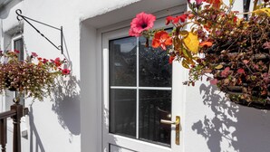 Una puerta blanca con una ventana, un timbre y macetas con flores en la pared.