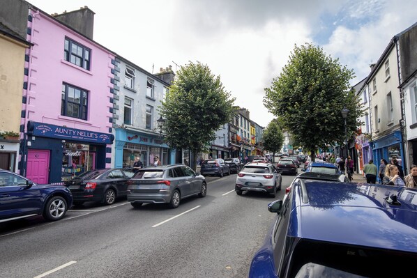 A street with cars parked on the side, buildings with shops, and pedestrians walking on the sidewalk. - No 12 Bridge Street Westport (Westport)