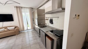 Een moderne keuken met een ingebouwde oven, een spoelbak en een fornuis. Er staat een beige bank met decoratieve kussens en een flatscreen televisie hangt aan de muur.