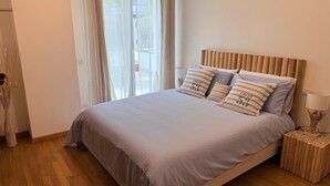 Een slaapkamer met een bed, kussens, een nachtkastje, een lamp en een raam met gordijnen.