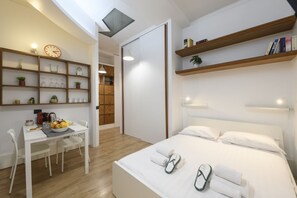 A modern hotel room with a bed, bedside tables, a desk with chairs, a dining area, and built-in shelves. - Visconti di Modrone, 18 - Small nest in central location (Milan)