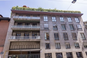 Ein mehrstöckiges Gebäude mit Balkonen, einer begrünten Dachterrasse und einem sichtbaren Eingangsbereich im Erdgeschoss.