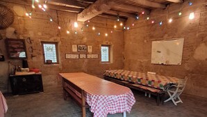 A rustic room with exposed wooden beams, a long table with a checkered tablecloth, a bench, and a small window with a view. - Ferme Berger-By, a family home in the heart of the 2 lakes region (Pressins)