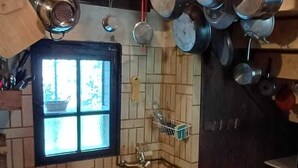 A kitchen with hanging pots, a window, and a tiled backsplash. - Ferme Berger-By, a family home in the heart of the 2 lakes region (Pressins)
