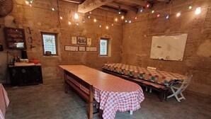 A rustic room with exposed wooden beams, a long table with a checkered tablecloth, and string lights. - Ferme Berger-By, a family home in the heart of the 2 lakes region (Pressins)