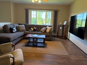 A living room with a sectional sofa, a coffee table, a TV, and a large window.