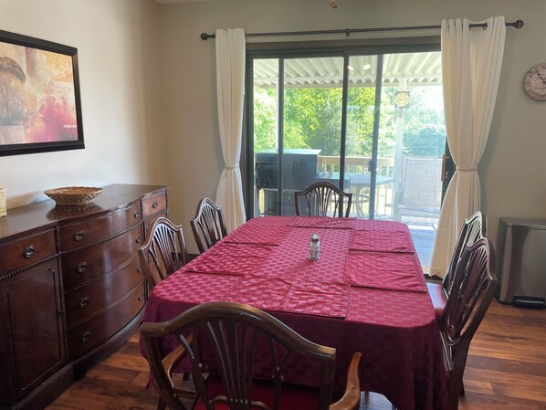 A dining area with a table set for four, wooden chairs, a wooden cabinet, and a view through a glass door to an outdoor patio.