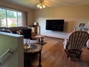 A living room with a sofa, a coffee table, a TV, a wooden floor, and a ceiling fan.