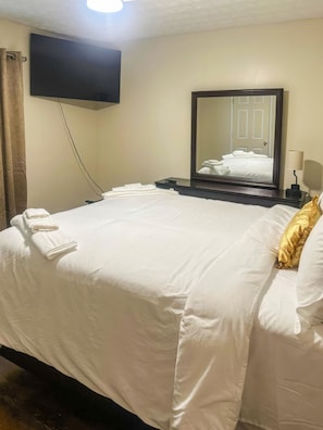 A hotel room with a bed, a flat-screen TV mounted on the wall, a bedside table with a lamp, and a large mirror. - Penny Cove - Stone Mountain (Stone Mountain)