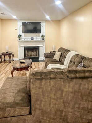 A living room with a brown sofa, a glass coffee table, a fireplace, and a TV mounted above it. - Penny Cove - Stone Mountain (Stone Mountain)