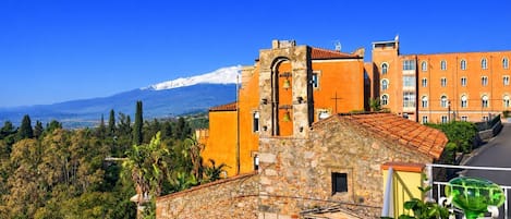 Un edificio de piedra con un campanario, un edificio de techo rojo y una montaña al fondo.