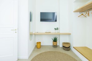 Une salle de bain moderne avec une porte blanche, un miroir, un téléviseur à écran plat, une étagère en bois, une petite plante et un tapis rond tissé.