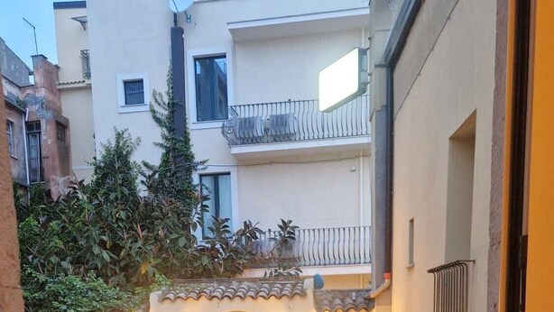 A courtyard with a staircase leading to a door, surrounded by buildings with balconies and potted plants. - House Awaya Taormina Cathedral - Villa (Taormina)