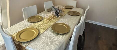 A dining room with a table set for four, white chairs, a chandelier, and a painting on the wall.