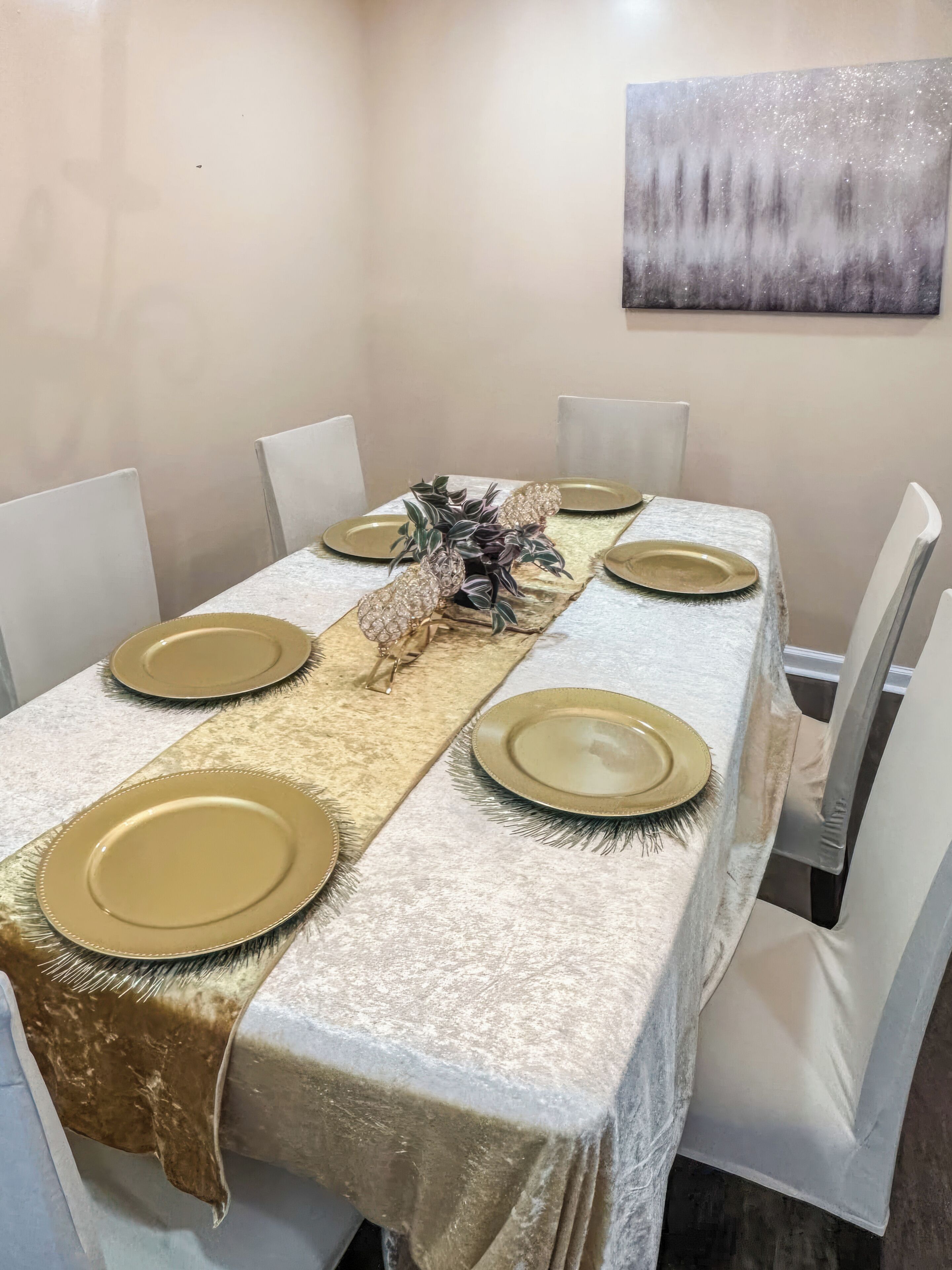 Una mesa de comedor dispuesta con platos dorados, un centro de mesa decorativo y un mantel con textura.