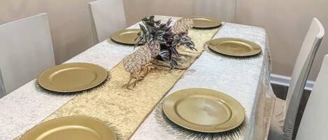 Una mesa de comedor dispuesta con platos dorados, un centro de mesa decorativo y un mantel con textura.