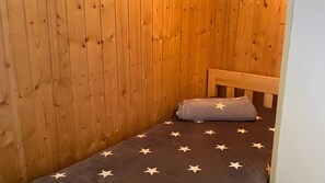 A small, wooden room with a single bed, a wooden headboard, and a wall with evenly spaced holes. - Holiday Home in Dranske (Dranske)