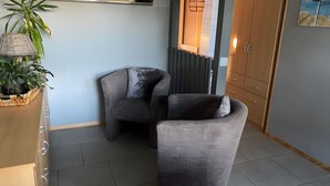 A corner room with a grey upholstered chair, a wicker plant holder, and a wooden cabinet. - Holiday Home in Dranske (Dranske)
