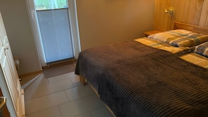 A bedroom with a bed, a wooden headboard, a bedside table, and a window with blinds. - Holiday Home in Dranske (Dranske)