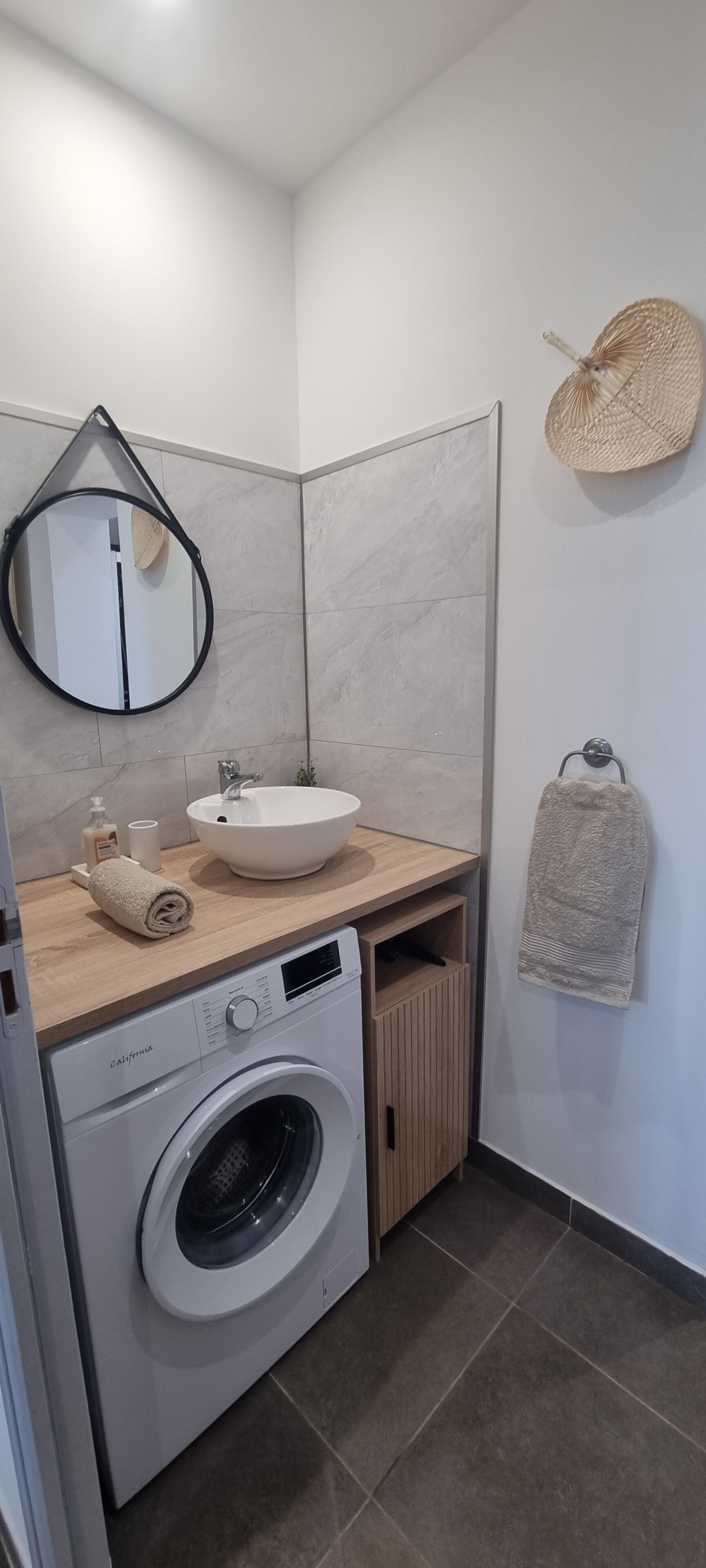 A modern bathroom with a round mirror, a sink, a washing machine, and a towel rack.