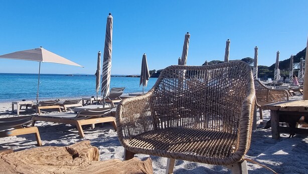 A beach with lounge chairs, umbrellas, and a wicker chair. - Villa Roccapina (Sotta)