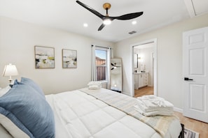 A bedroom with a bed, a ceiling fan, a window, and a door leading to a bathroom. - Furnished 4BR Home in Richardson - Extended Stays (Richardson)