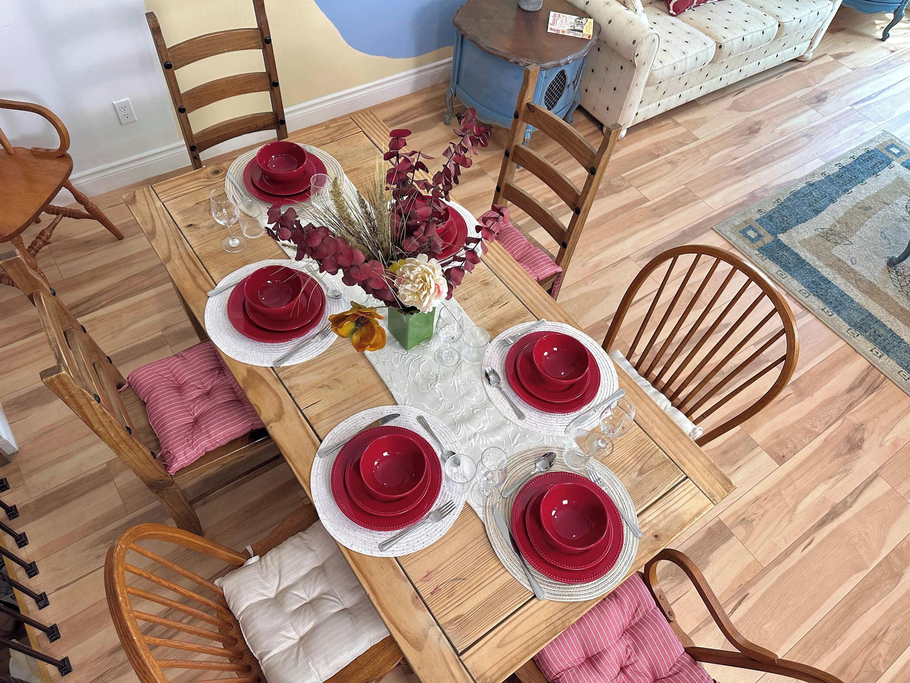 A dining table set with red plates, white napkins, and a vase with flowers.